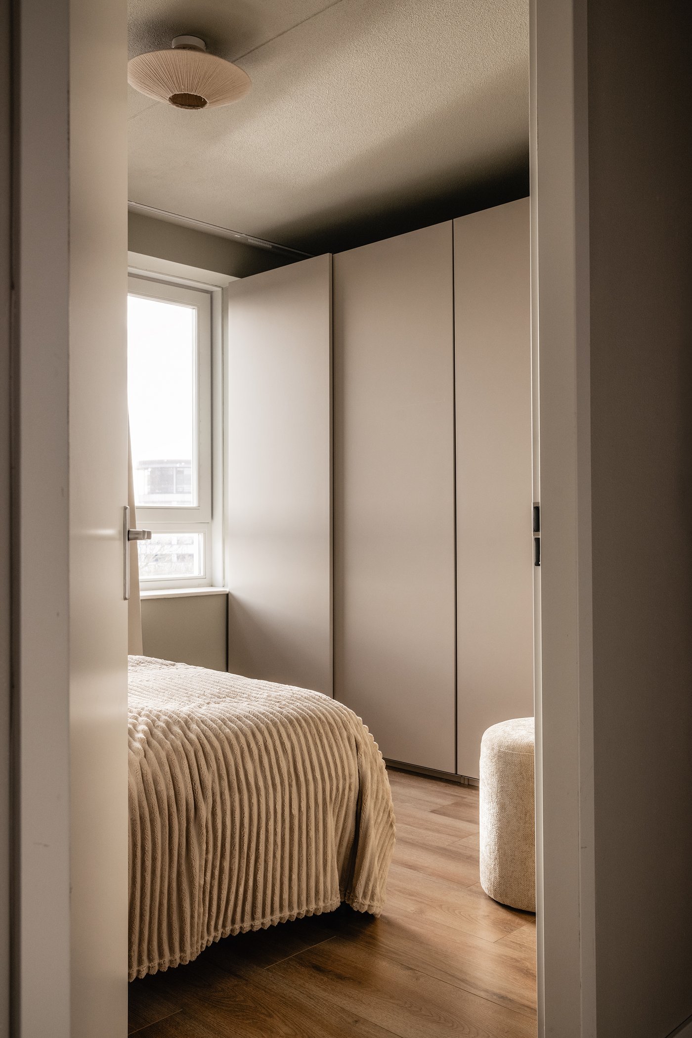 Slaapkamer met beige PAX kledingkast en bed met beige plaid erover.