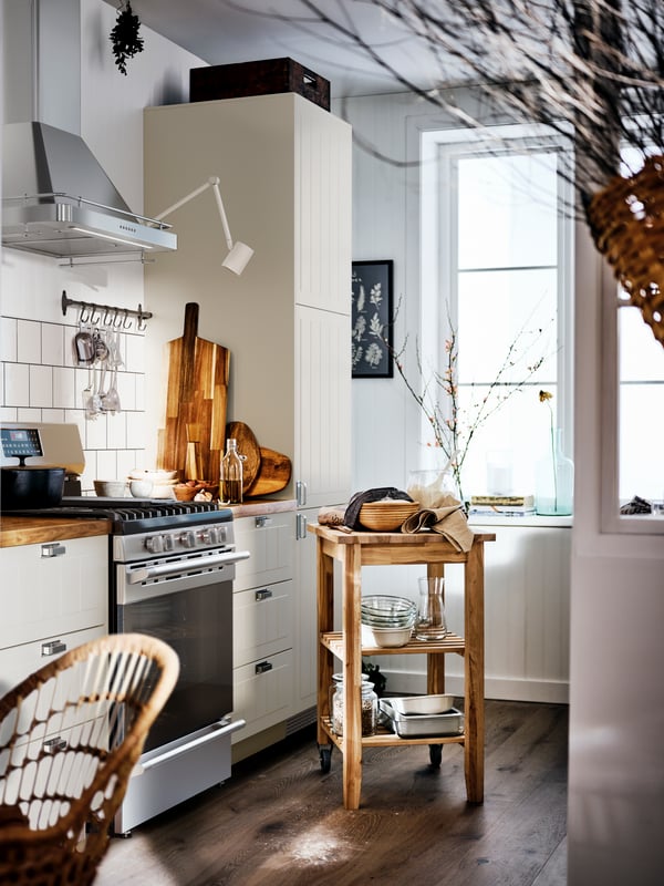 A beige country-style kitchen with a wooden worktop and white cabinets, and a BEKVÄM trolley in the middle of the room.