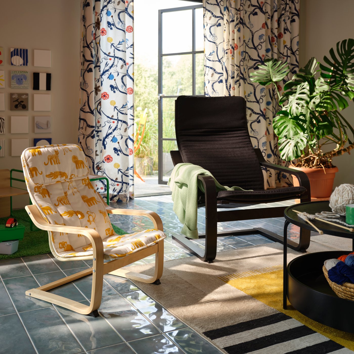 A black-brown POÄNG armchair next to an animal-patterned smaller POÄNG armchair in a room with plants and patterned curtains.