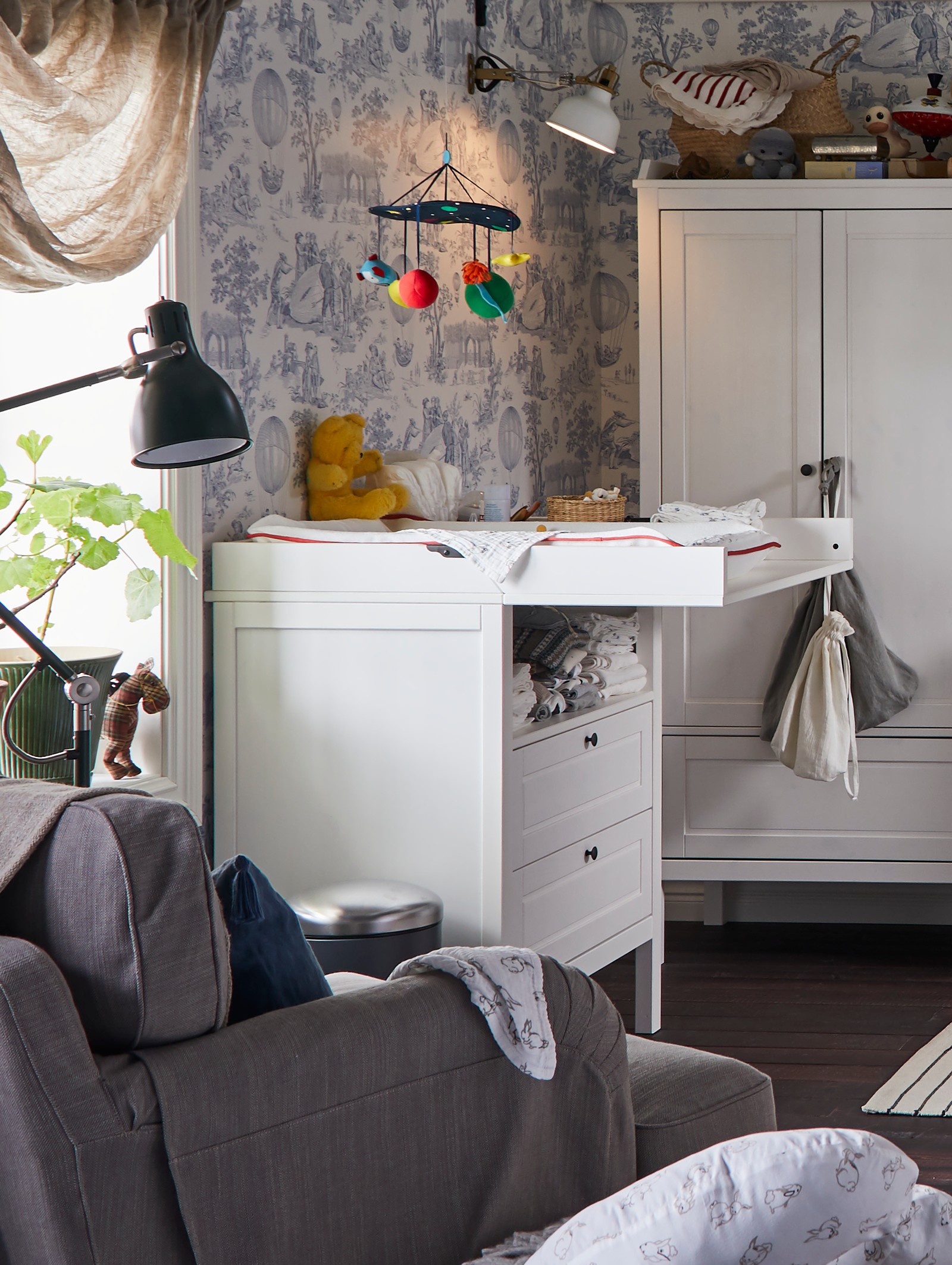 SUNDVIK sto za povijanje/komoda s fiokama, s KLAPPA visećom vrteškom, pored prozora u dečjoj sobi.