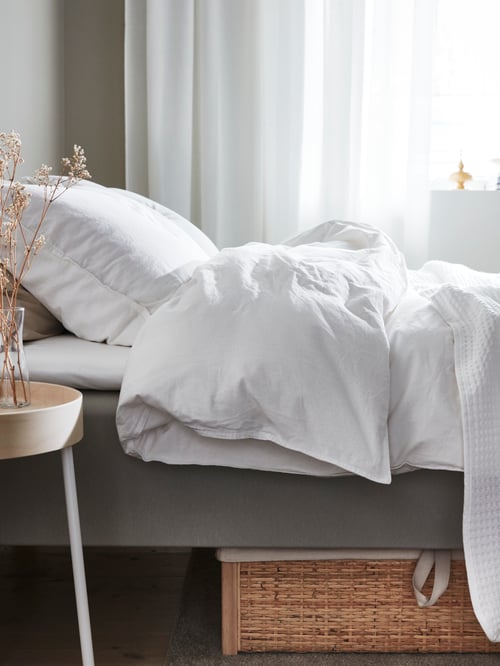 Chambre à coucher avec housse de couette blanche et 2 taies d’oreiller en coton, placées à côté d’une table d’appoint ronde.