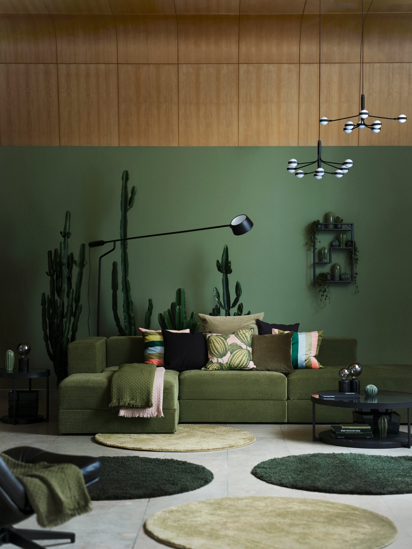 A modern living room featuring a green JÄTTEBO modular sofa with PARKSALLAT cushions and multiple carpets on the floor.