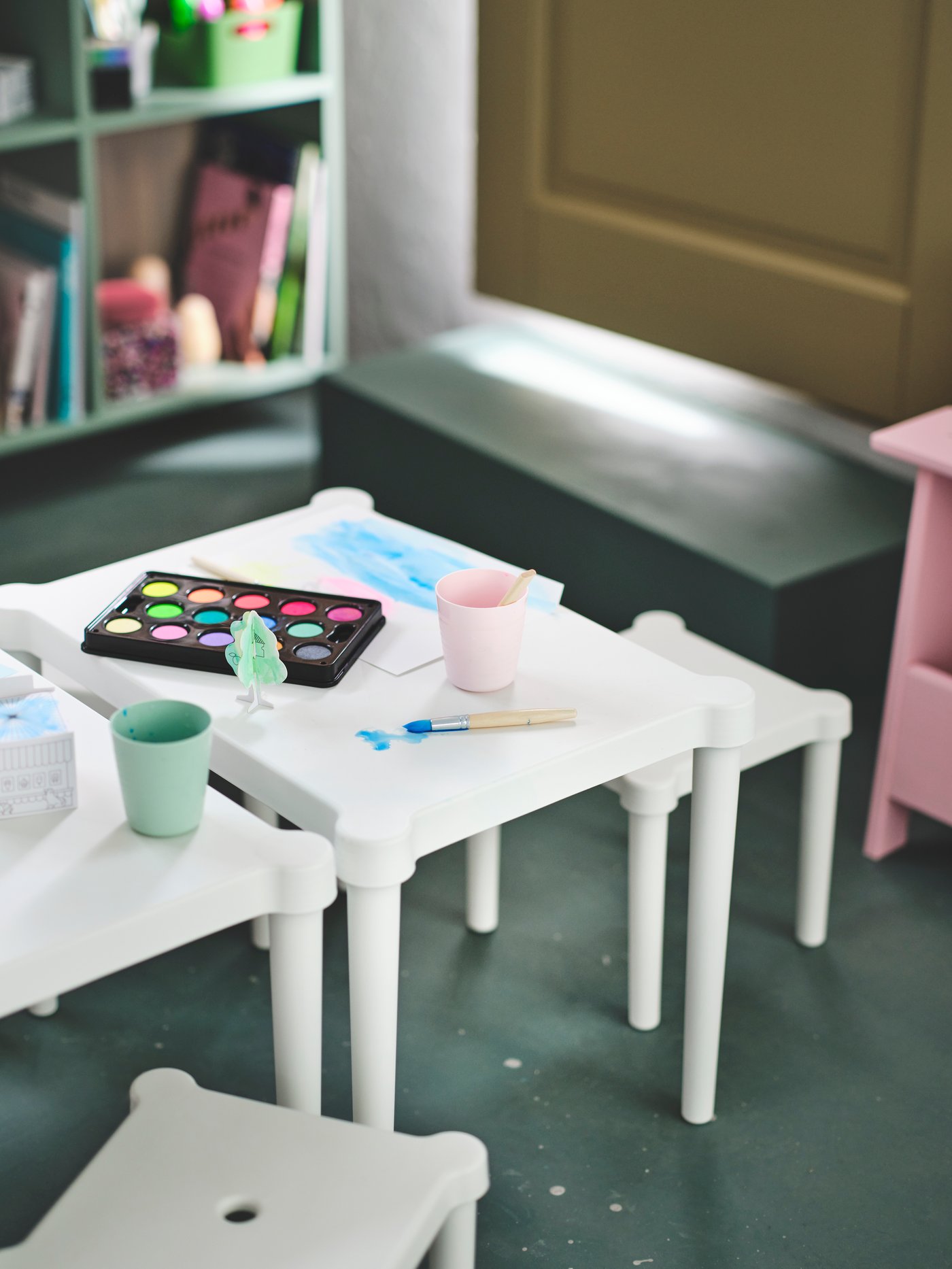 Dos mesas y un taburete infantil con material de manualidades encima.