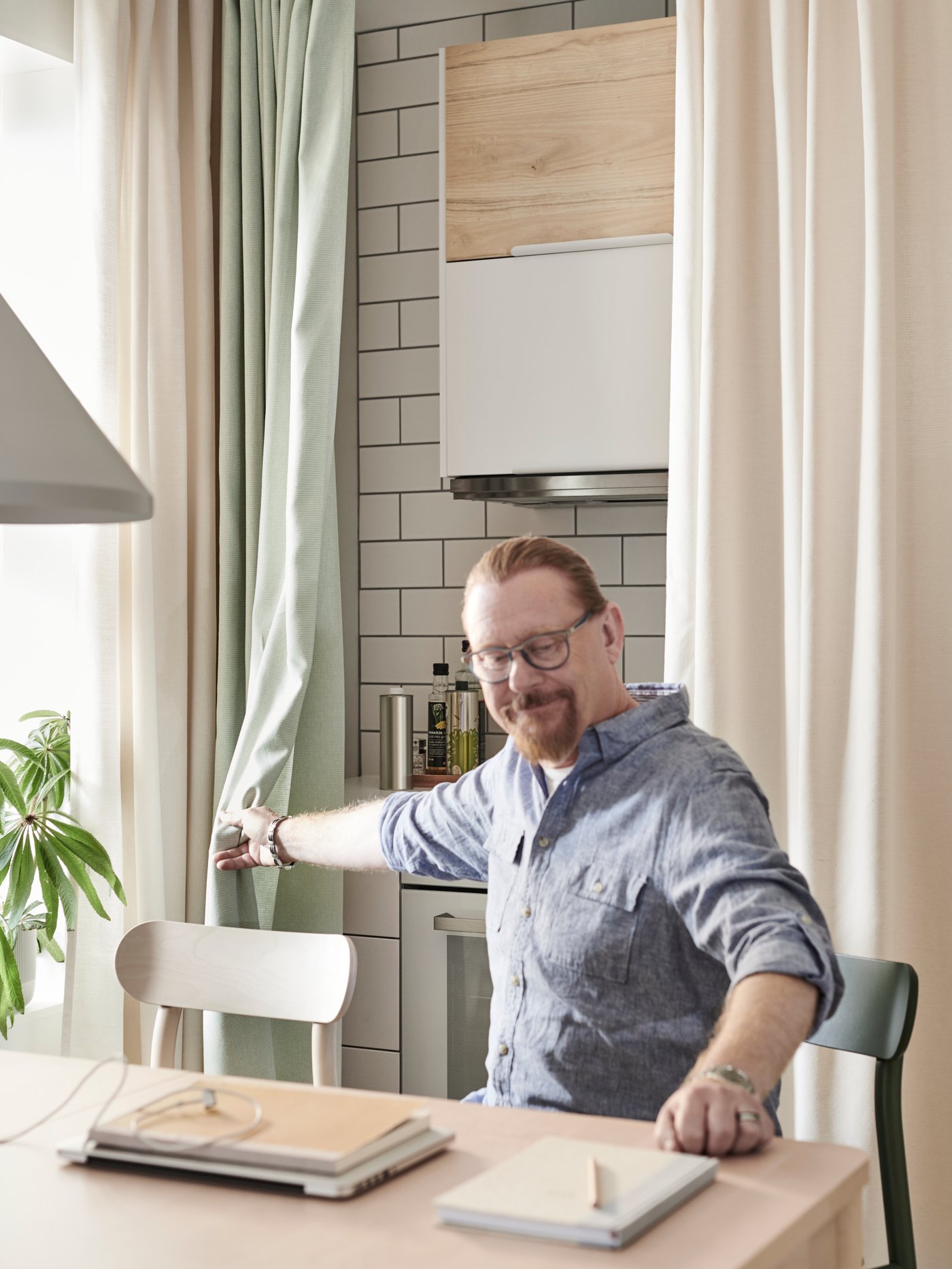 A man using his kitchen as an office slides the green and white MOALINA curtains to hide the kitchen top and stove.