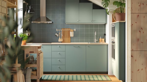 A kitchen has base and wall cabinets with matt grey-green NICKEBO fronts and a RESARÖ mobile drop-leaf table with storage.