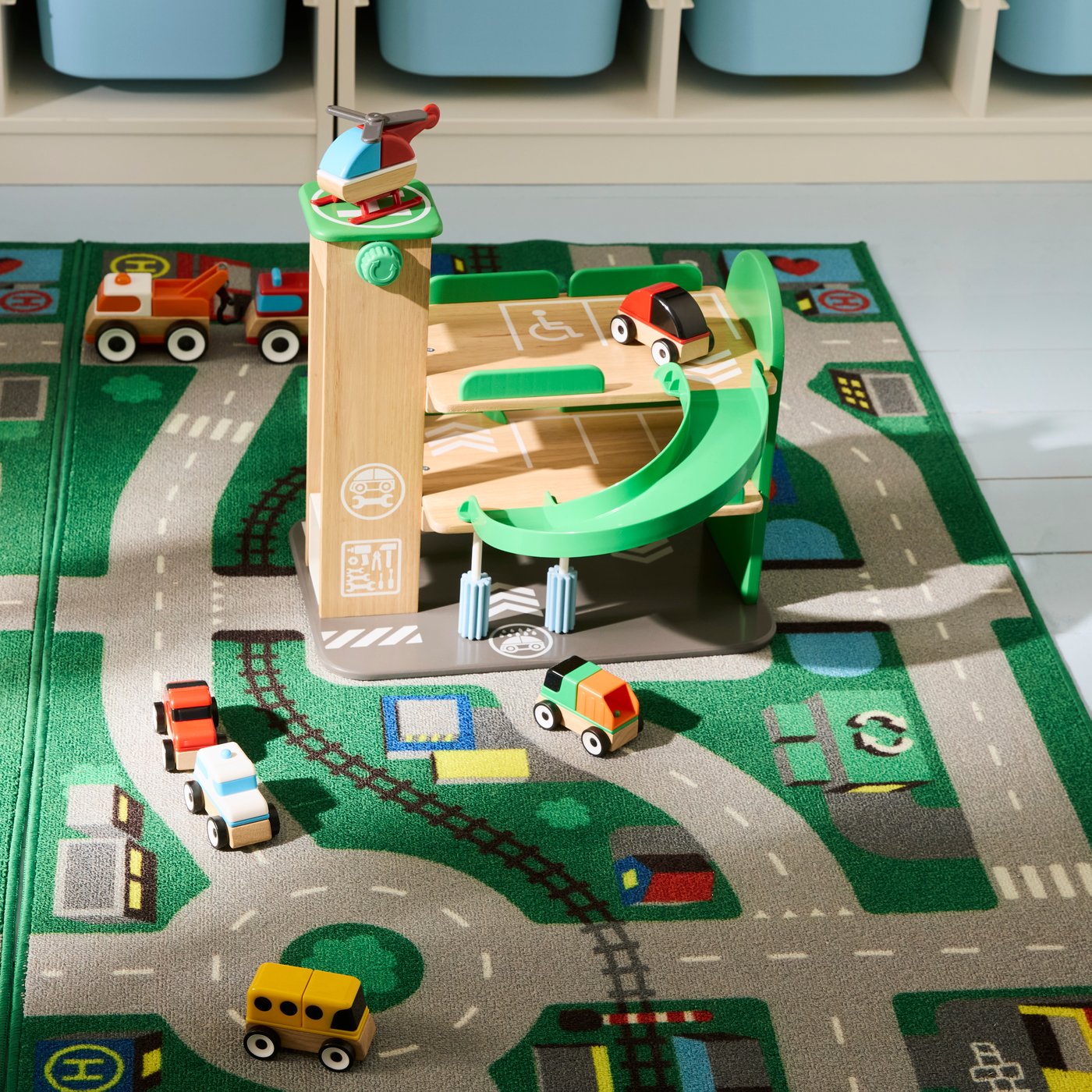 Colorful toy cars and a wooden parking garage set on a play mat with roads and tracks.