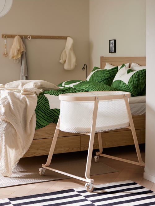 Bedroom featuring a beige ÄLSKVÄRD bassinet with mattress placed next to a TONSTAD bed frame with storage.