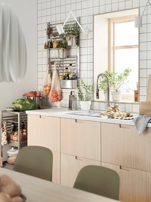A kitchen with FRÖJERED bamboo drawer fronts and two KUNGSFORS wall grids with herbs and jars in containers and net bags.