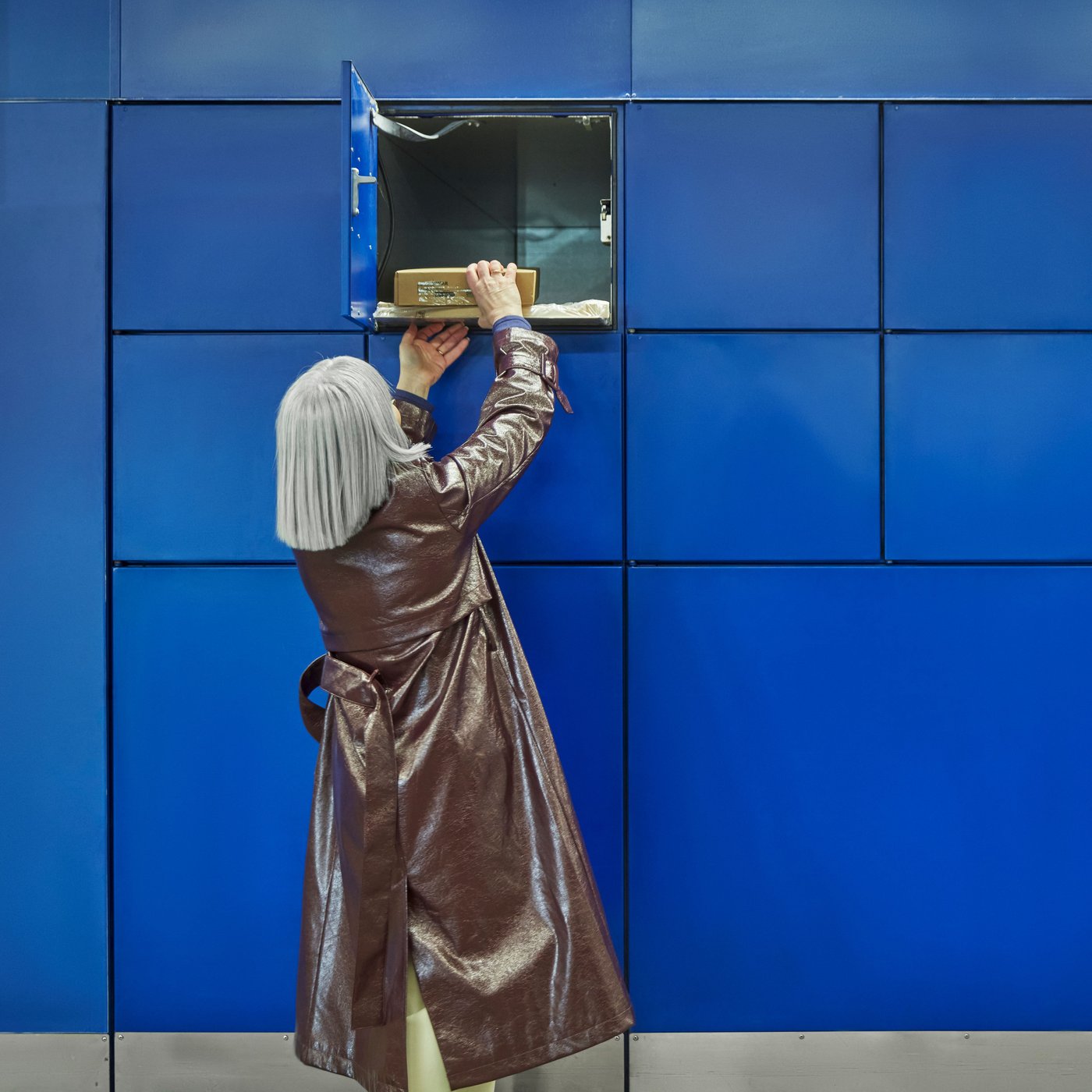 A person removing a parcel from a wall of blue collection lockers.