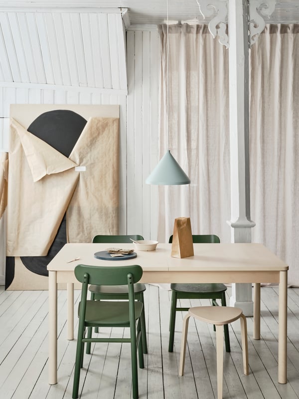 RÖNNINGE extendable table in light birch and rounded legs placed in a dining context with chairs around in a light room.