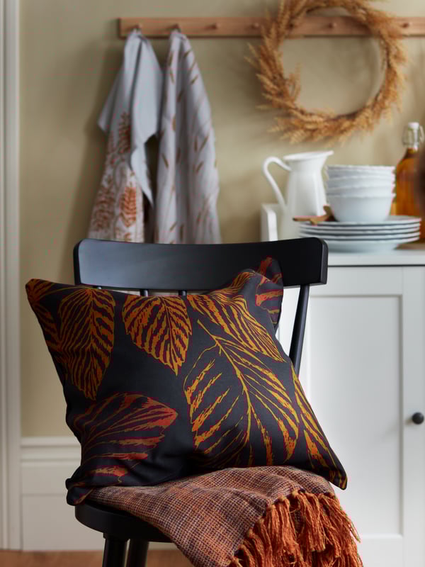 A black and red HÖSTKVÄLL cushion cover with inner cushion and orange HÖSTKVÄLL throw are set on a black NORRARYD chair.