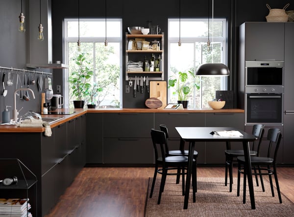 Vue d’une grande cuisine en forme de I avec des façades foncées et un plan de travail en bois ainsi qu’une table et quatre chaises