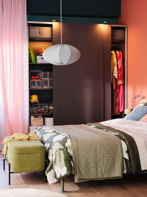 Un clóset PAX/HASVIK gris oscuro con las puertas corredizas que se abren detrás de una cama cubierta con un juego de cobija GETRUTA con peso blanco/verde.