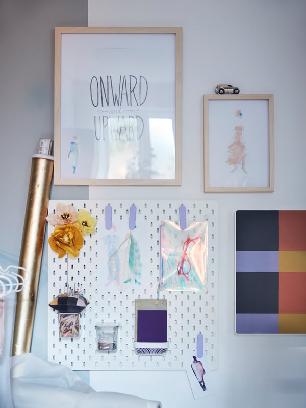 A light wall section with drawings in RÖDALM frames next to a white SKÅDIS pegboard holding decorations and accessories.
