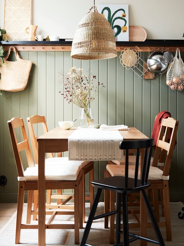 An antique stained pine HÄGERNÄS table and 4 chairs and a black AGAM junior chair stand in a small cottage-style dining area.