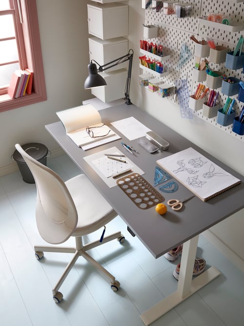 A neat and tidy workspace with a grey desk and white office chair and a pegboard with containers on the wall.
