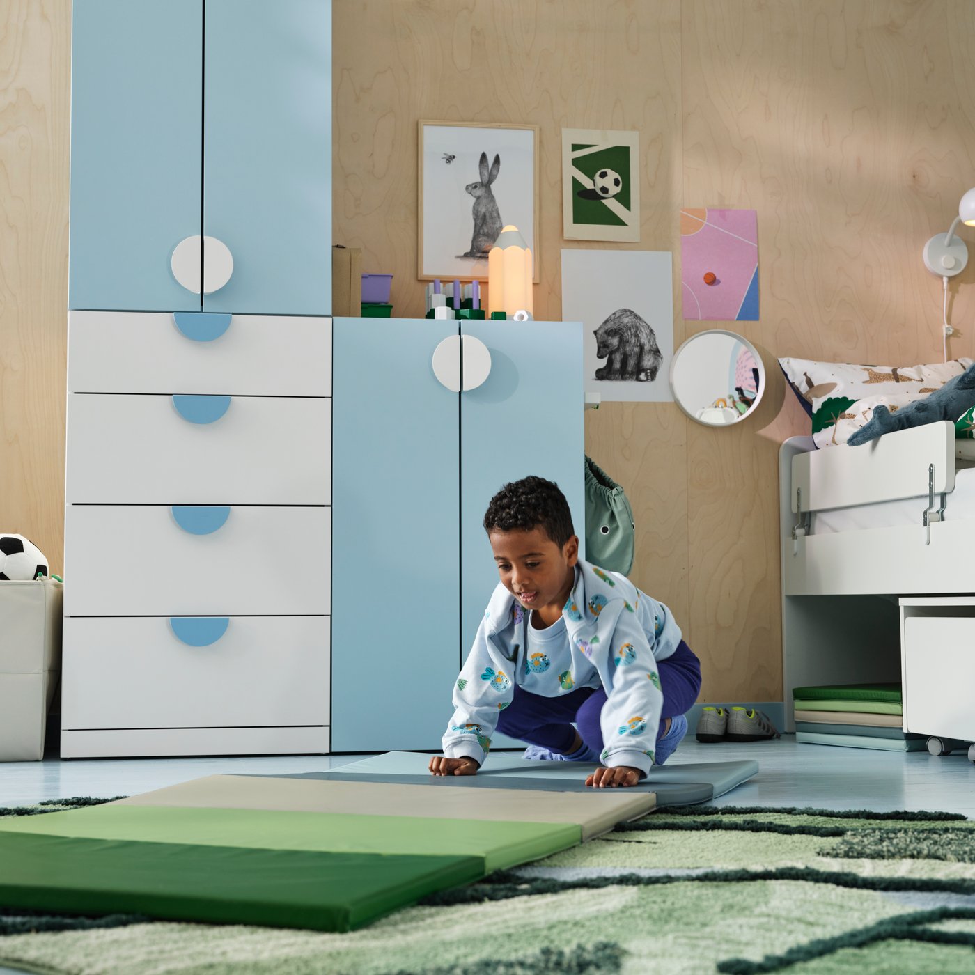 A child on a blue/green mat in a room with a light blue and white LASTARE storage combination, animal posters on the wall.