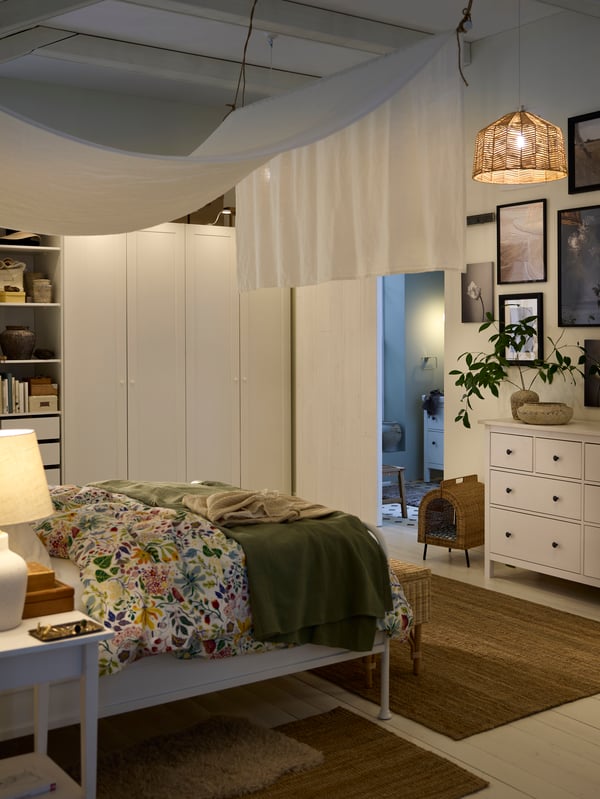 A bed covered in STRANDLUMMER bed linen and a green bedspread in front of a PAX/GULLABERG wardrobe in a dimly let bedroom.