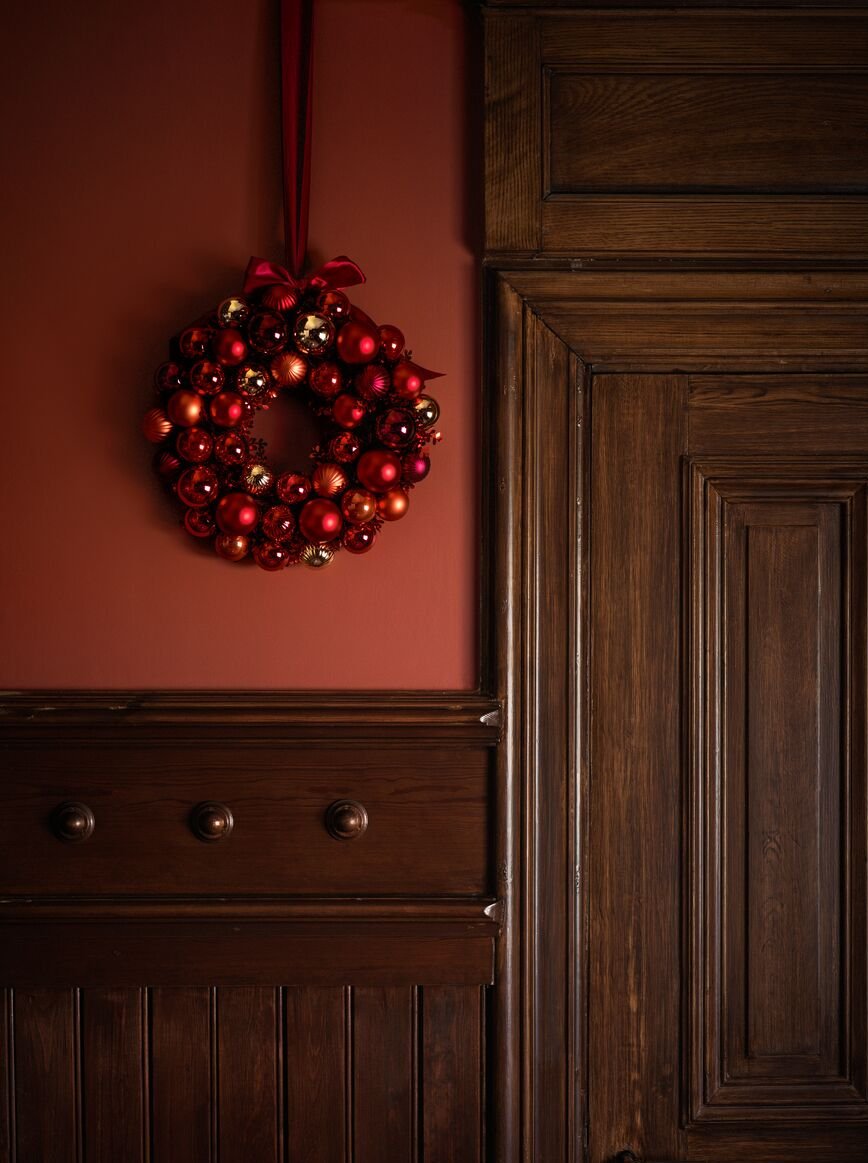 Červený věnec lesklých kouliček visí na červené zdi vedle velkých, tmavě-dřevěných dveří zdobených dekorativními výliskami.