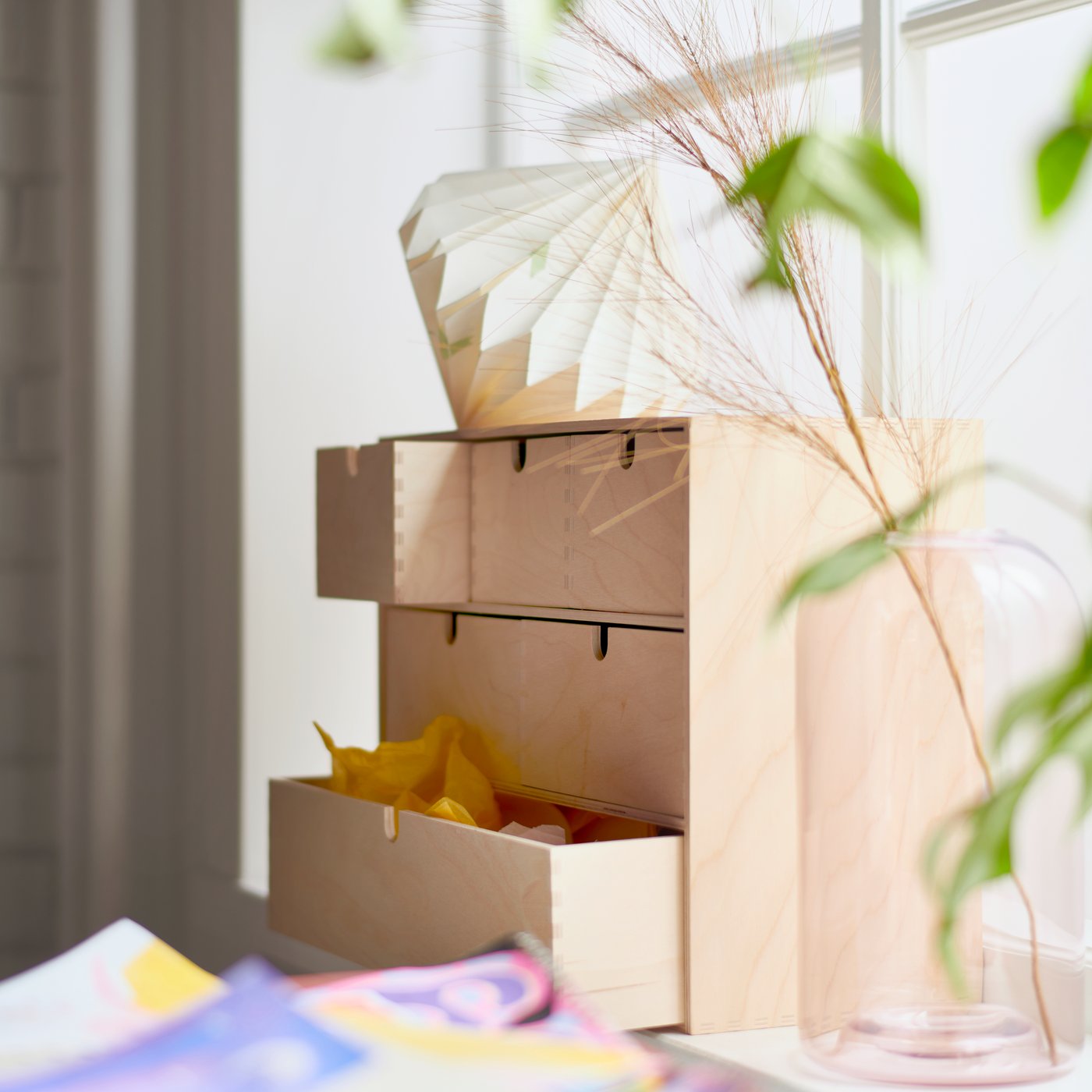 Wooden MOPPE mini chest of drawers on a window ledge with folder paper and a vase with plant beside.