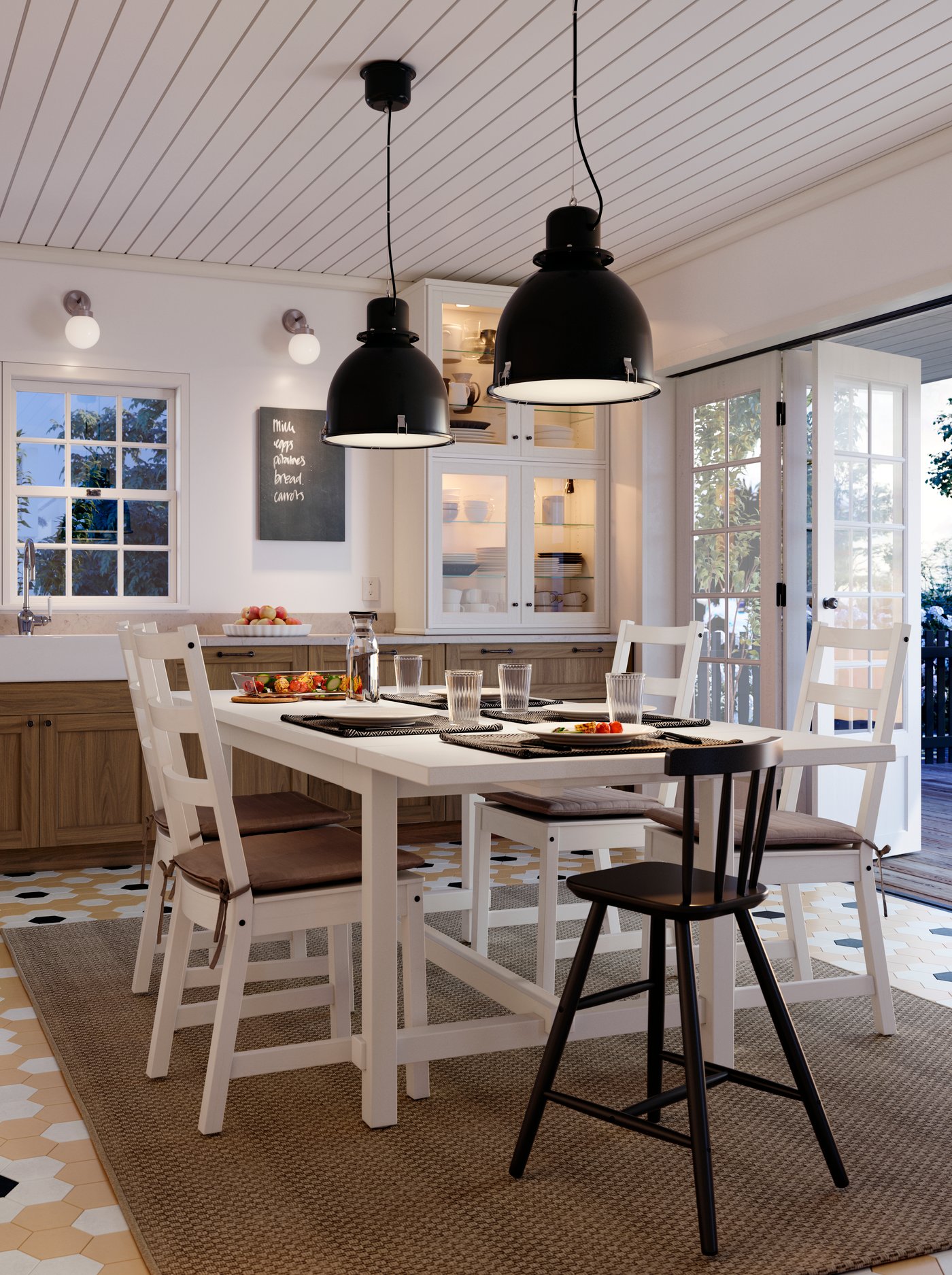 Una mesa NORDVIKEN blanca con cinco sillas para comer en mitad de una cocina. Hay dos lámparas de techo SVARTNORA colgadas del techo.