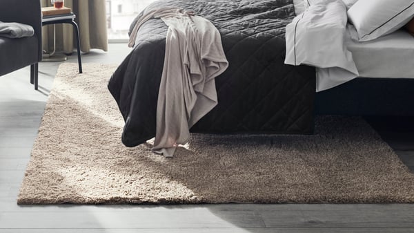 Ein VINDEBÄK Teppich Langflor in hellbeige, 200x300 cm liegt unter einem Bett. 