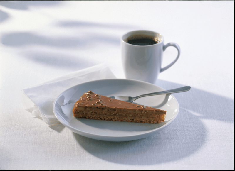 Part de gâteau au chocolat servie sur une assiette blanche avec une tasse de café noir sur une table claire.