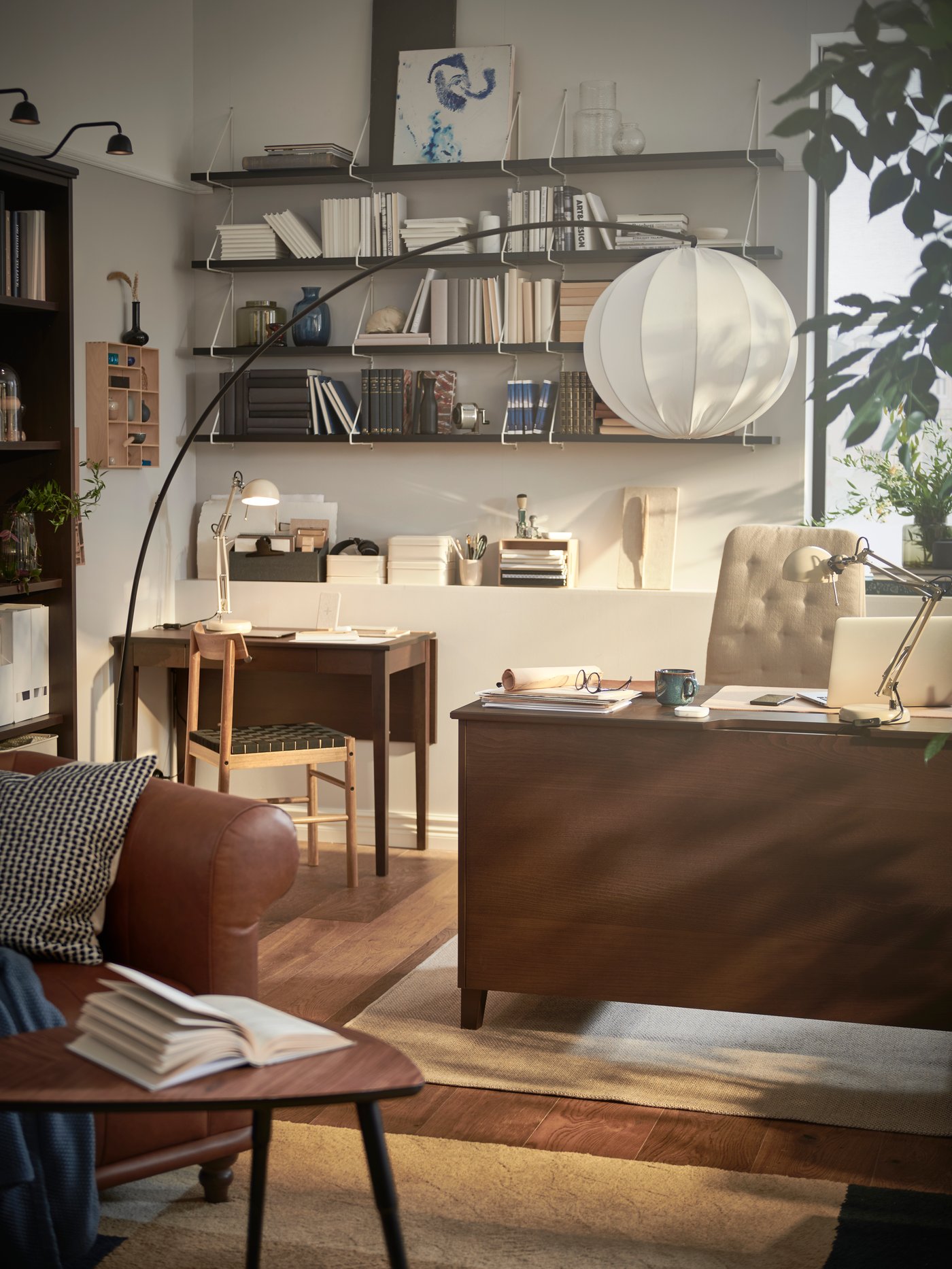 Un salón con un escritorio IDANÄS con una silla de reuniones y una lámpara de pie colocada a su lado, y una mesa de ala abatible IDANÄS.