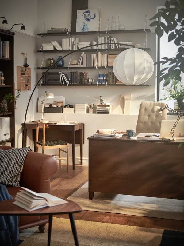 A refined and stylish room features plenty of shelves on the walls with neatly arranged books and two spots to work from.