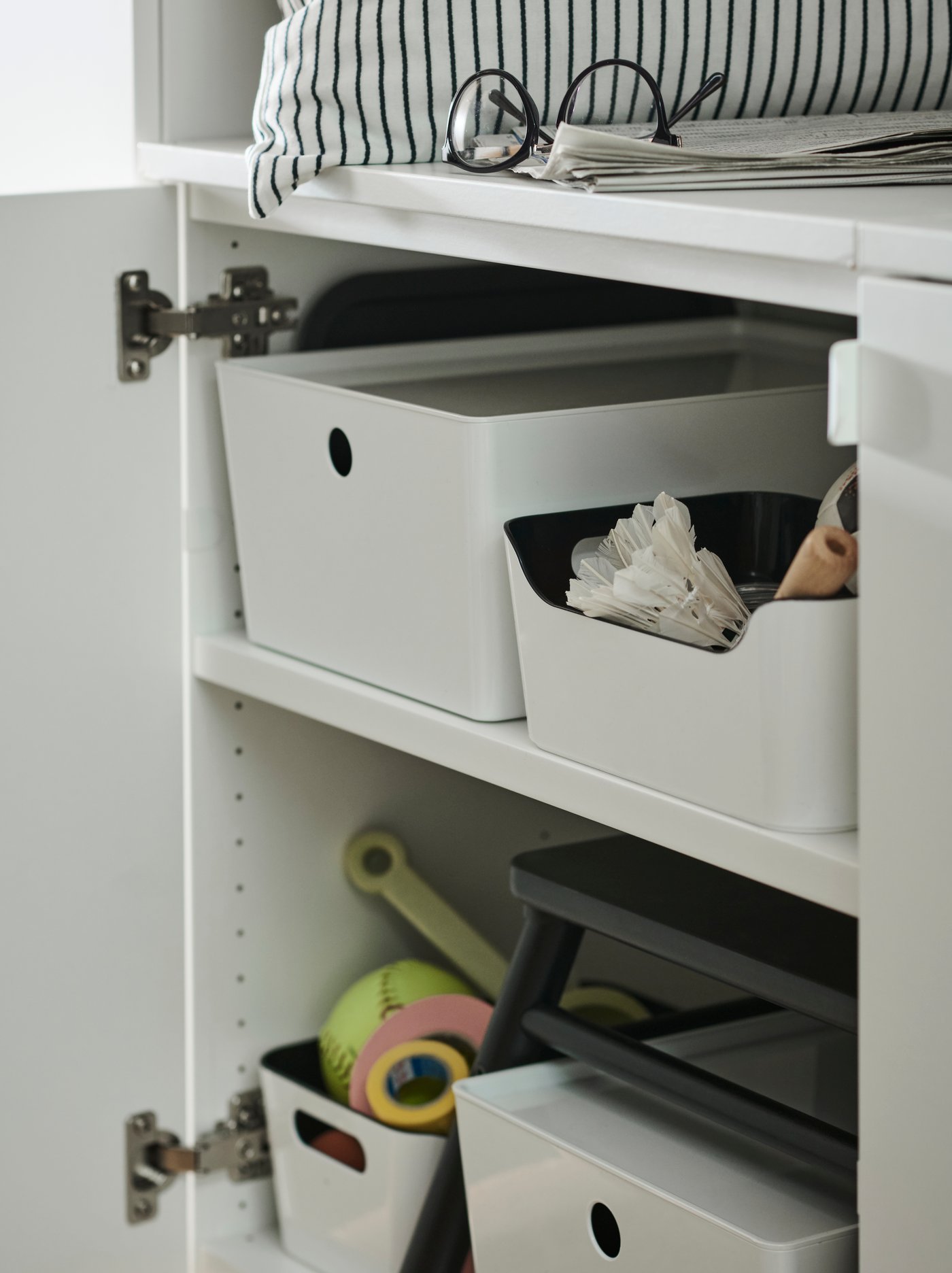 Un mueble con su puerta abierta y en el interior se ven dos repisas con cajas KUGGIS blancas. Una está tapada y las otras muestran artículos en el interior.