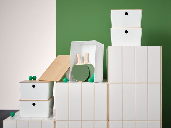 A collage of a storage furniture and white KUGGIS storage boxes with a green and white wall in the background.