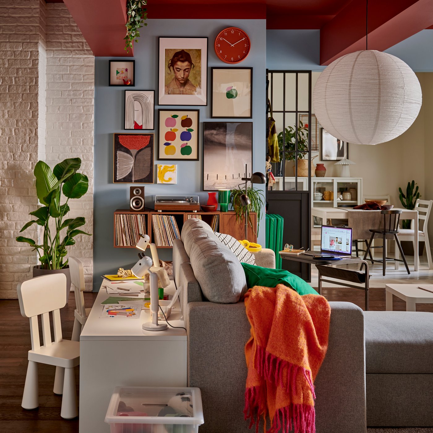 Ett vardagsrum med en livfull vägg med inramad konst, kompletterat med en grön växt och en ljusgrå BLODFLÄDER bild.