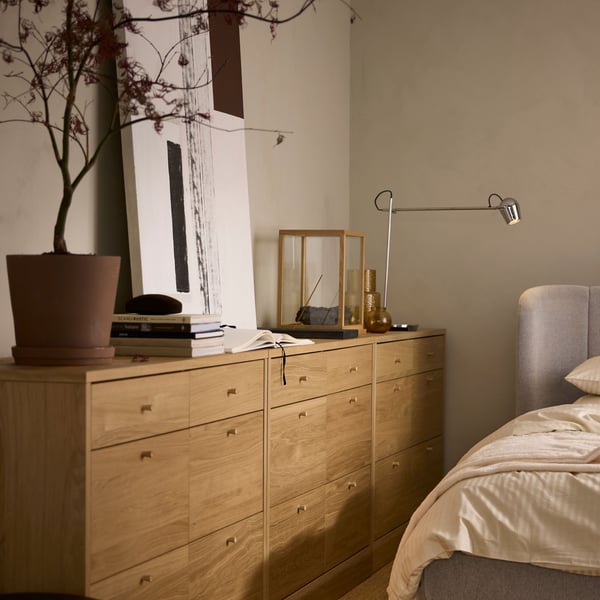 Tre TONSTAD byråer med 6 lådor längs en beige vägg, med en MODERMOLN lampa och en växt i en KLARBÄR kruka med fat.
