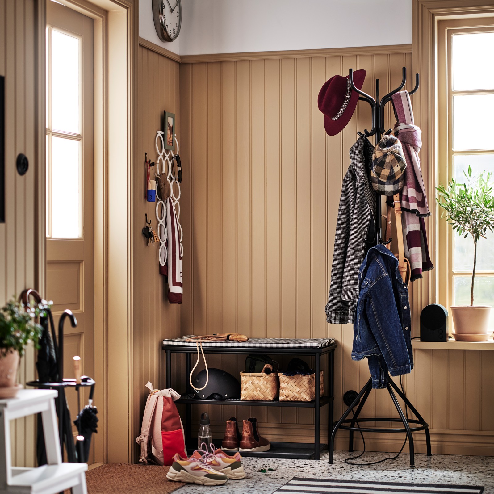 A black NIPÅSEN hat/coat stand holding coats and jackets is beside a black NIPÅSEN bench with shoe storage holding footwear.