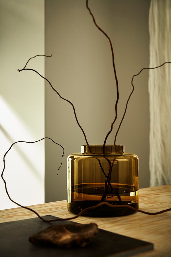 A small single KONSTFULL vase in green glass with twigs inside. 