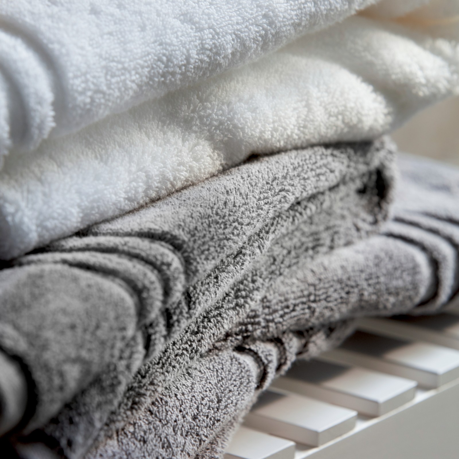A close-up of white bench with folded grey BROKGLIM bath towels, showing its dense cotton and decorative woven stripes.