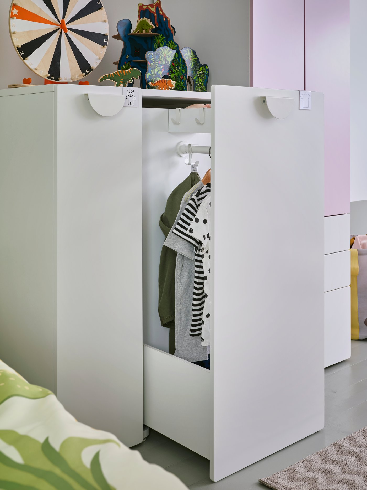 A SMÅSTAD wardrobe with a pull-out unit stands open. Hooks and a clothes rail with clothes on hangers are inside.