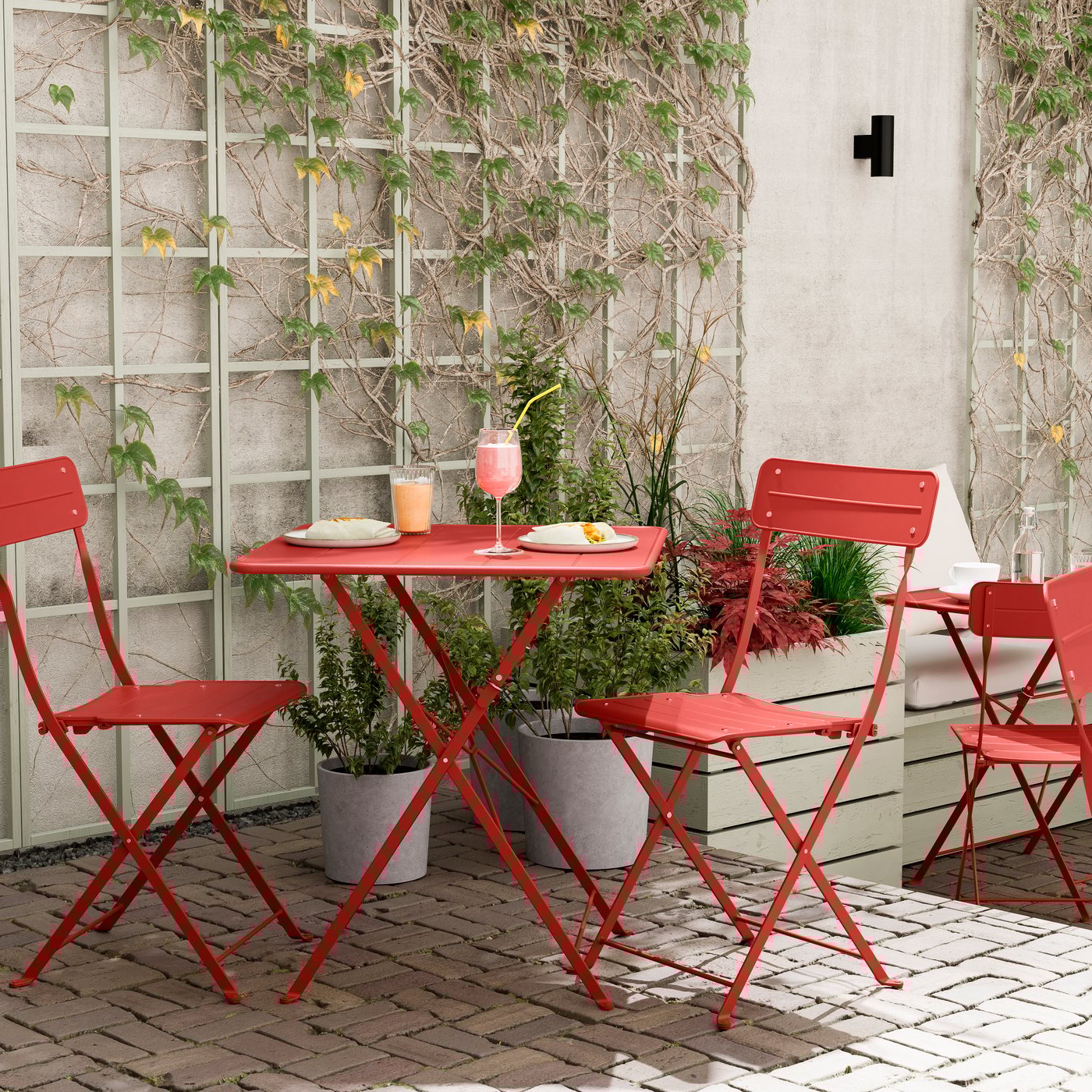 An outdoor bright red/bright red SUNDSÖ table and 2 folding chairs outside