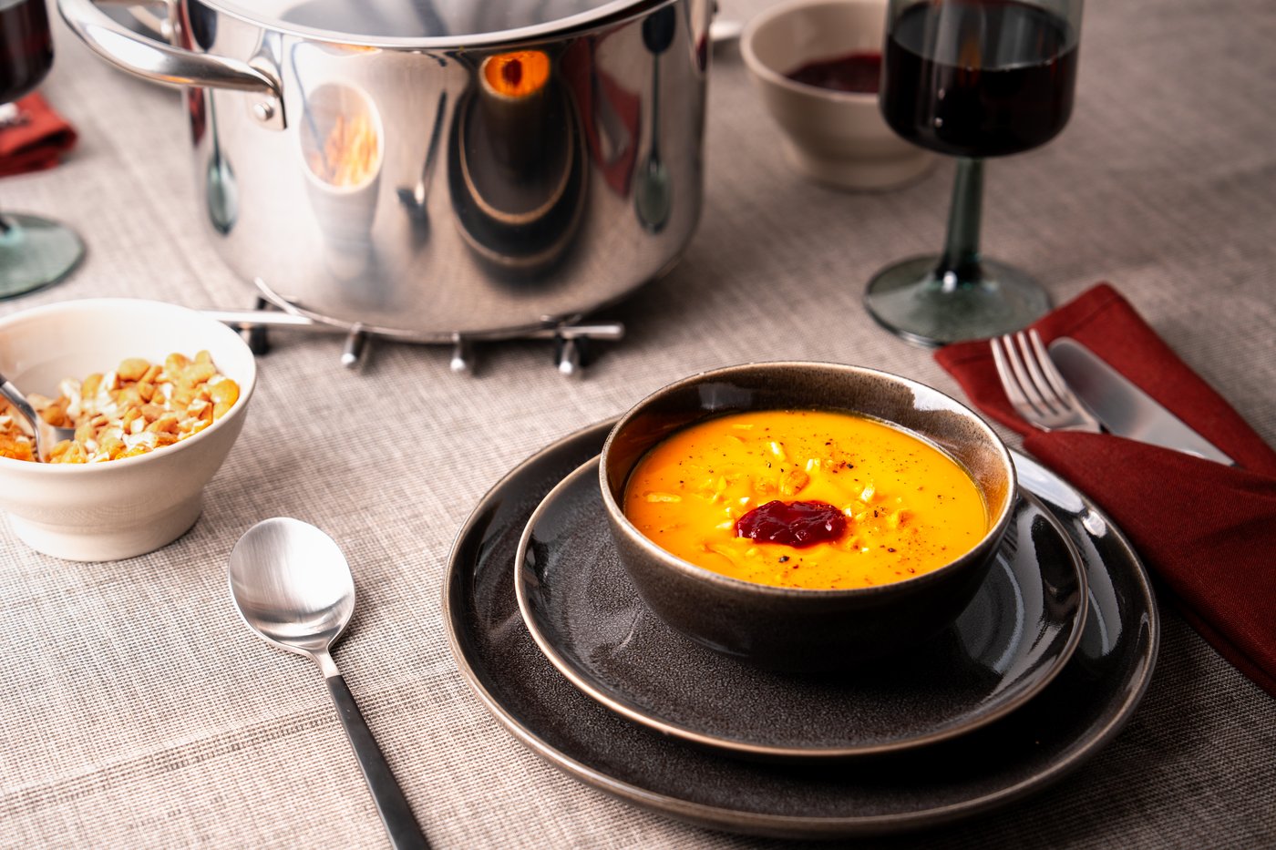 Eine Kürbissuppe, angerichtet in einer schwarzen Schale und einem schwarzen Teller.