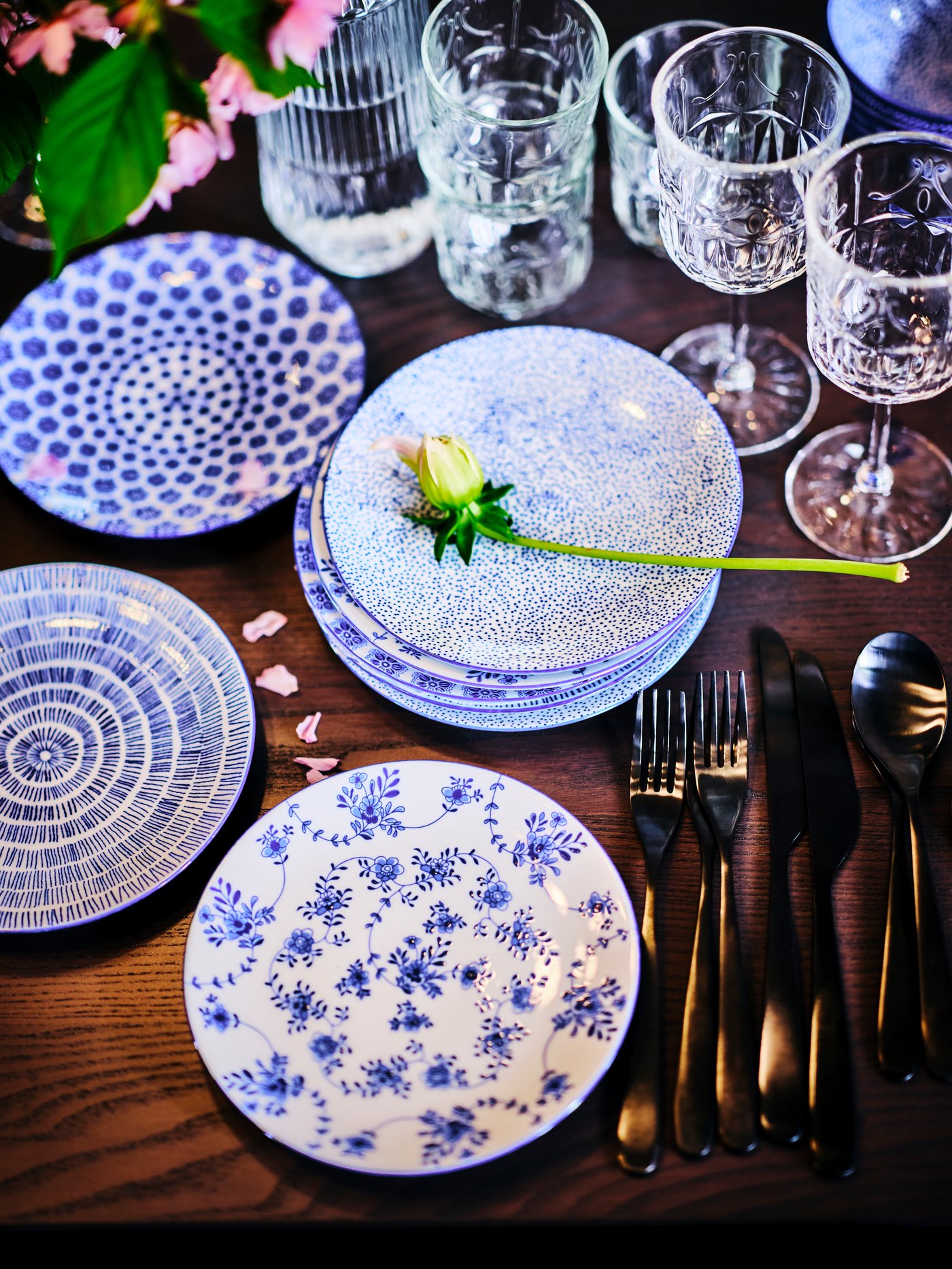 A collection of ENTUSIASM side plates on a wooden table, with cutlery, drinking glasses and SÄLLSKAPLIG wine glasses.