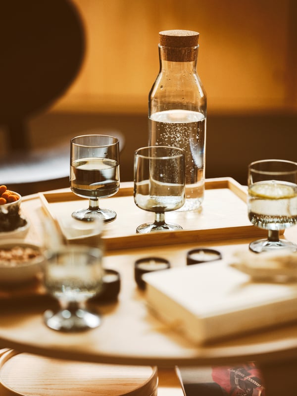 An IKEA 365+ carafe with stopper containing water and four OMBONAD goblets, two with water, placed on a OSTBIT tray.