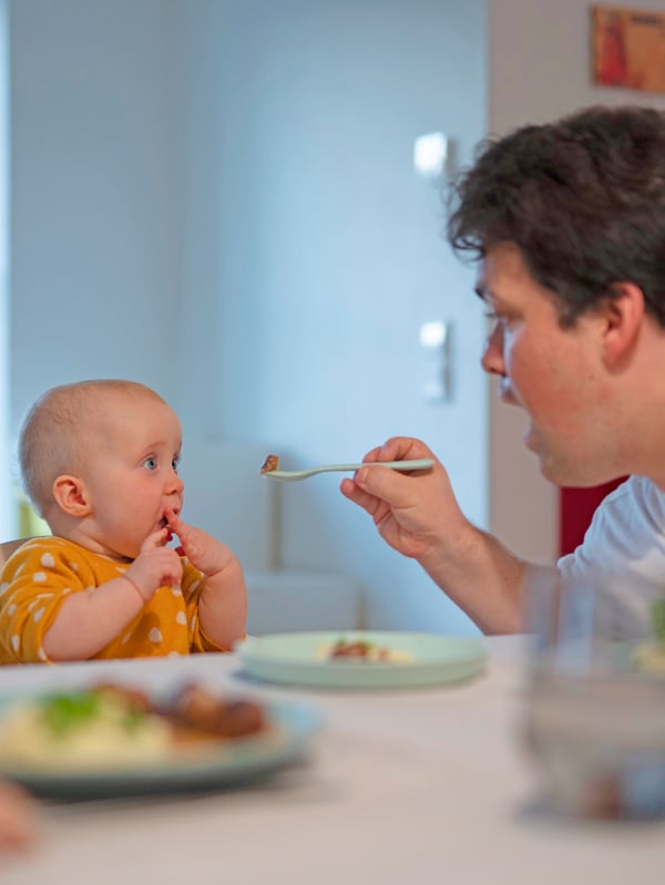 Father feeding a baby placed in an ANTILOP high chair next to a dining table.
