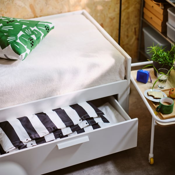 Close-up of BRIMNES bed with storage box underneath pulled out, showing folded black/white striped duvet cover.