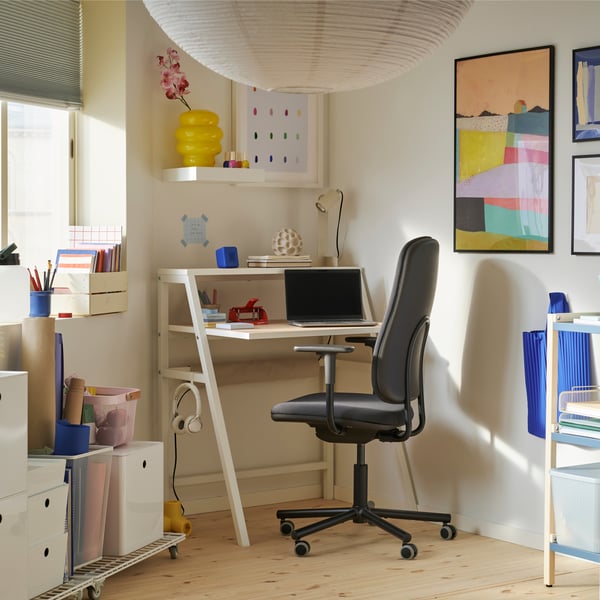 Canto com janela e espaço de trabalho pequeno com secretária MITTPLAN, cadeira giratória, estante aberta e arrumação com rodízios.