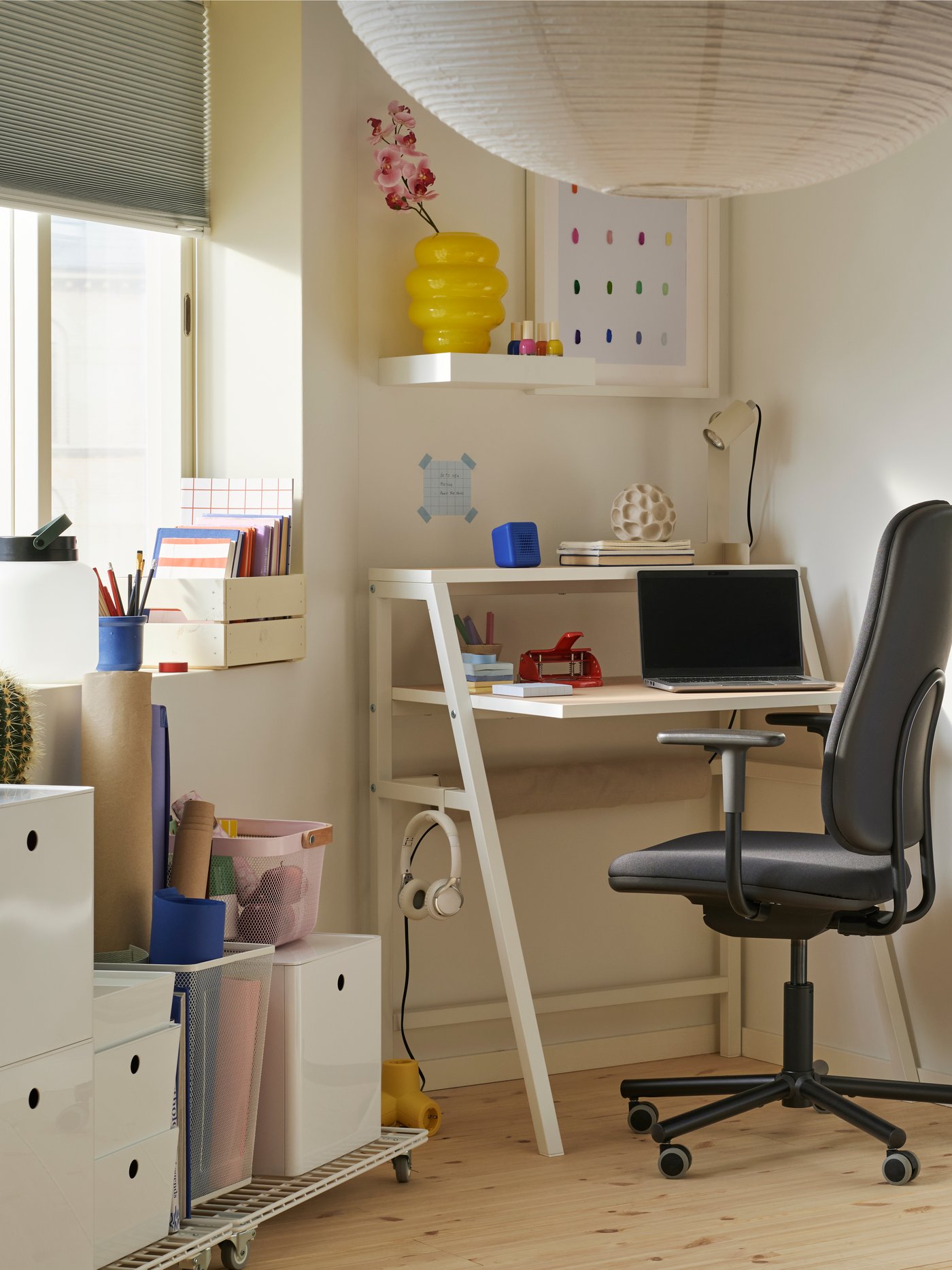 A corner with a window and a small workspace with a MITTPLAN desk, an office chair, open shelving, and storage on castors.