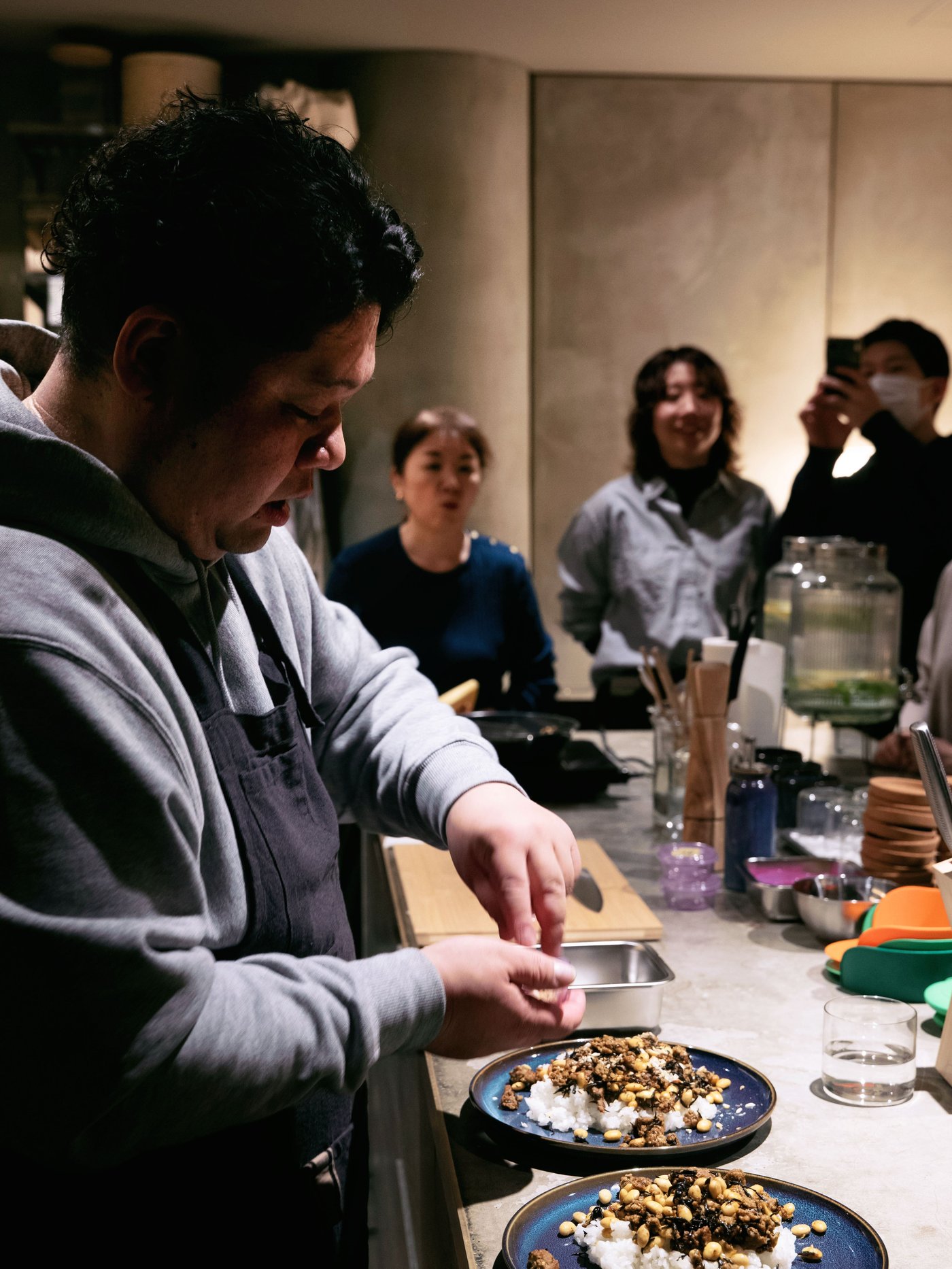 キッチンカウンターを囲んで食事を楽しむ人たちと、その奥に座って会話する人たち
