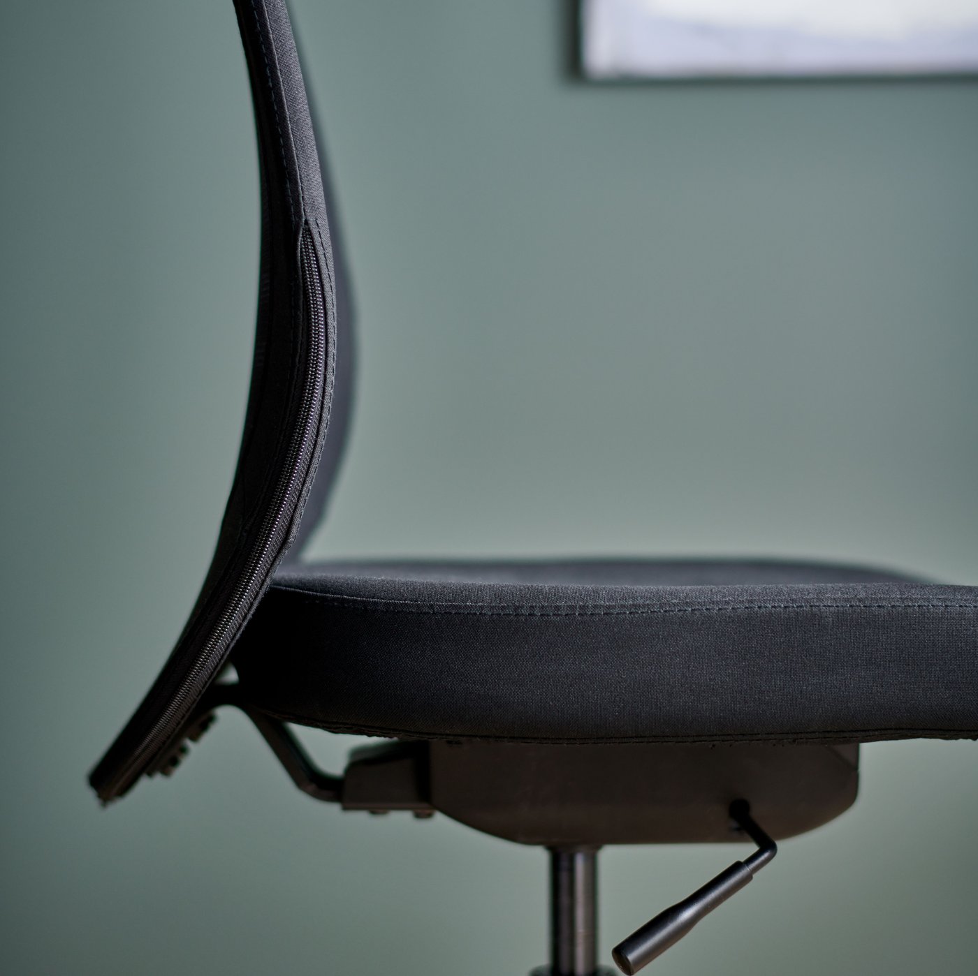 مقعد ومسند ظهر لكرسي مكتب FLINTAN أسود، مع إطار صورة على الحائط الأخضر خلفه.