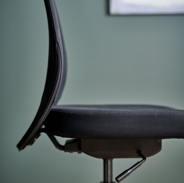 The seat and backrest of a black FLINTAN office chair, with a picture frame on the green wall behind it.