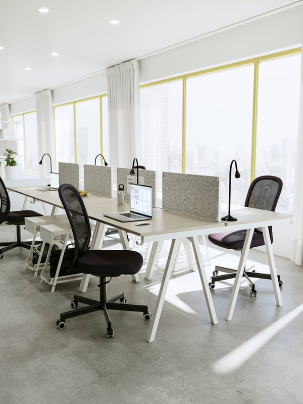 A row of beige/white desks and black chairs facing each other with TROTTEN notice boards as dividers for privacy.