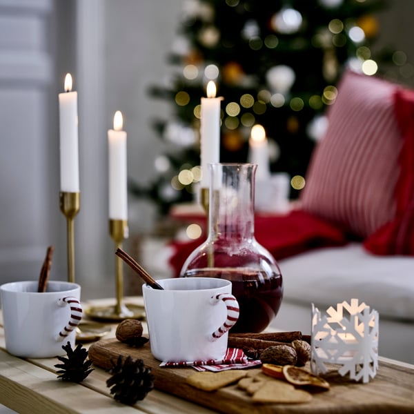Två VINTERFINT muggar och en karaff är fyllda med VINTERSAGA fruktdryck med glöggsmak och står på ett festligt juldukat bord.